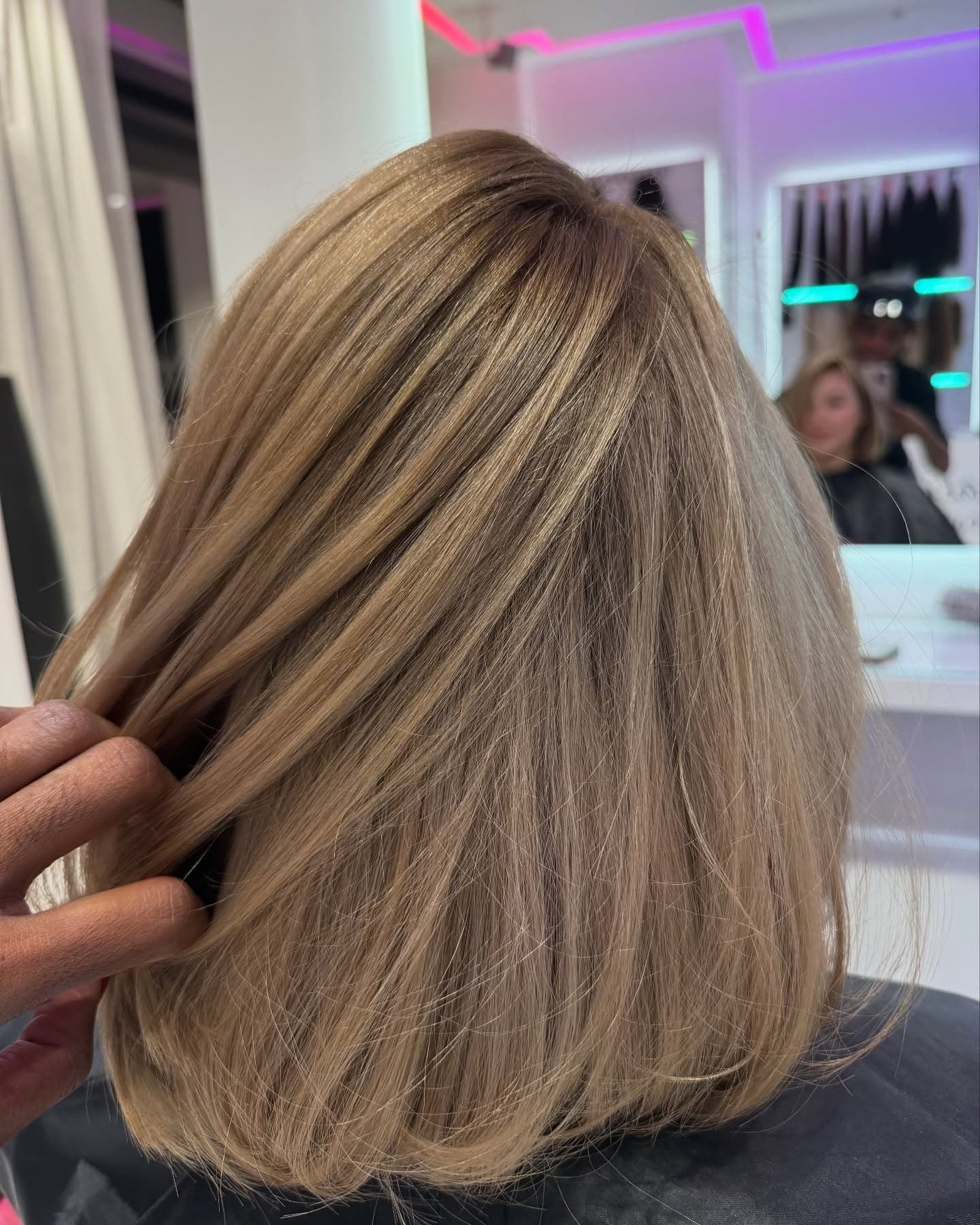 Bob in Bronde, eine Hand hebt eine Strähne an